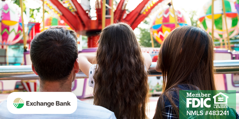 Image shows two adults and a child looking over a barrier at a fair ride